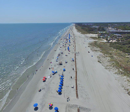 shoreline beach with umbrellas and people with pipeline