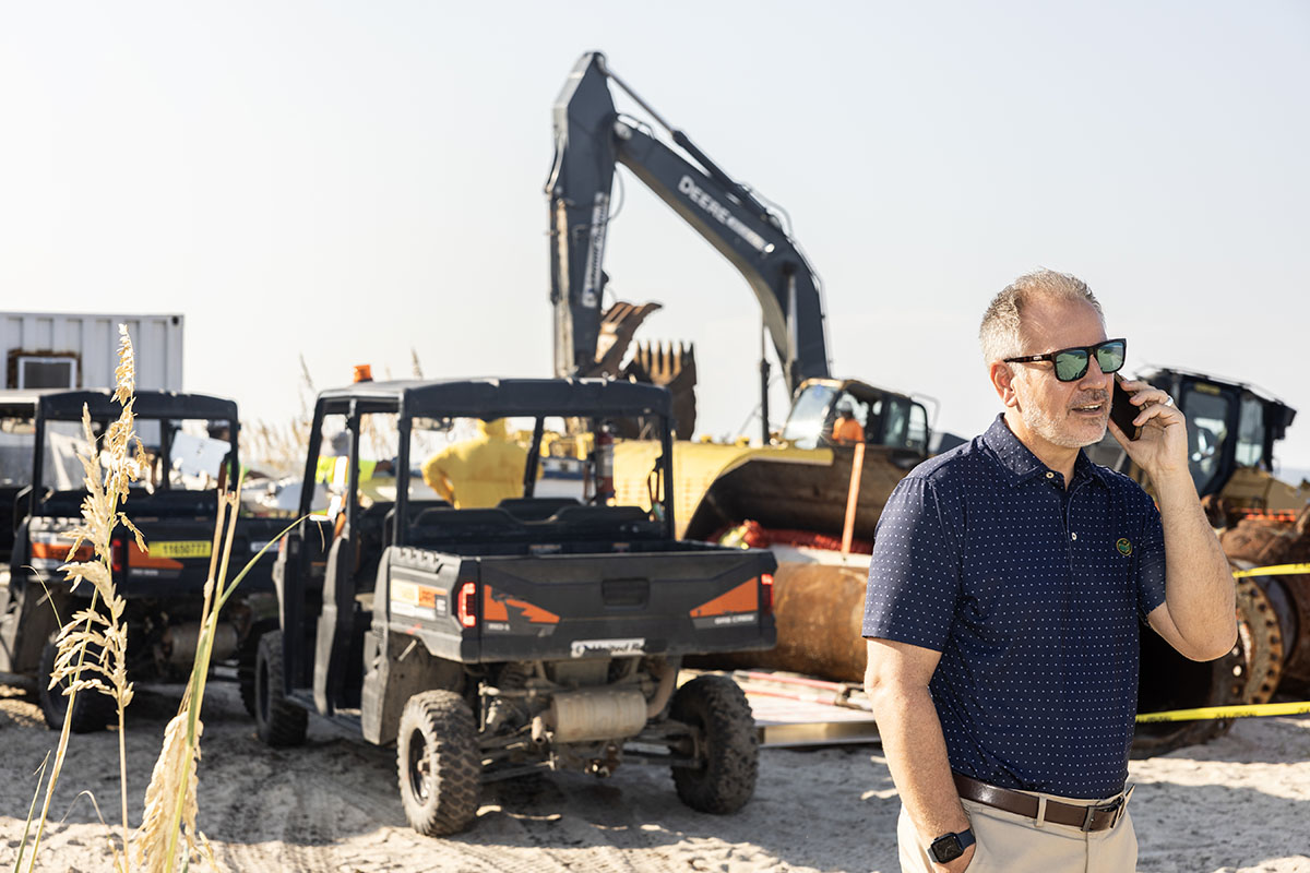 Marc Orlando on cell phone in front of construction equipment on the beach