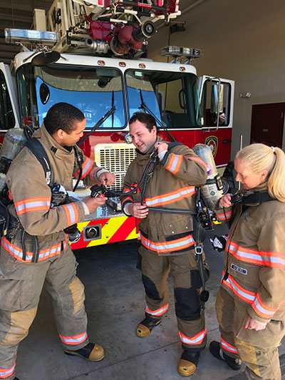 3 firefighters in gear in front of fire truck