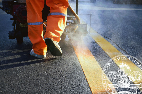 Contruction worker legs pushing machine painting lines on road with Town logo