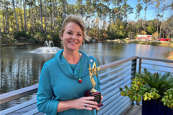 April Akins holding award on deck in front of lagoon